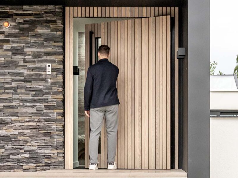 Pivoting wooden front door made of weathered ash wood and vertical glass