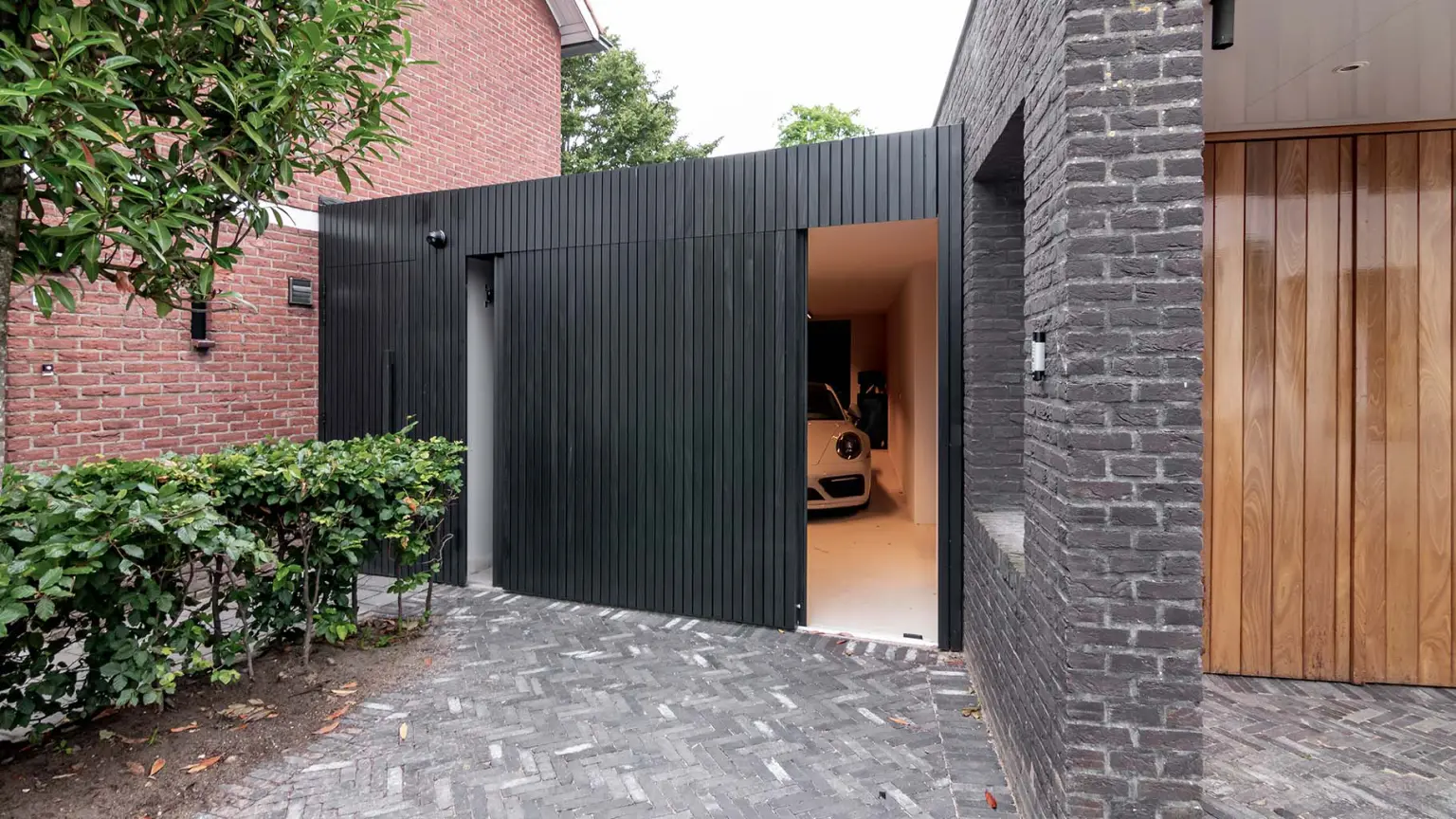 Modern garage with a black Afrormosia side sliding garage door and a Porsche